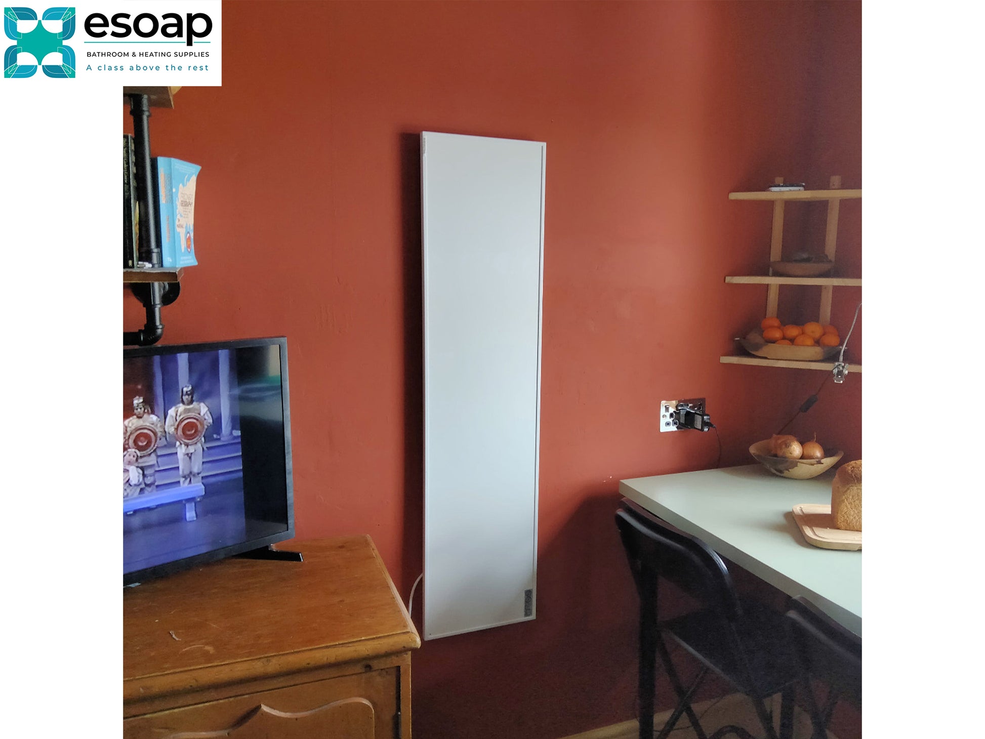 700W Classic Infrared Heating Panel Black on an orange wall with a television and wooden cabinet in the foreground.